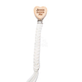 White braided baby pacifier clip featuring a wooden heart engraved with the words Jesus Loves Me, attached to a metal clip on a clean white background, designed for babies and toddlers