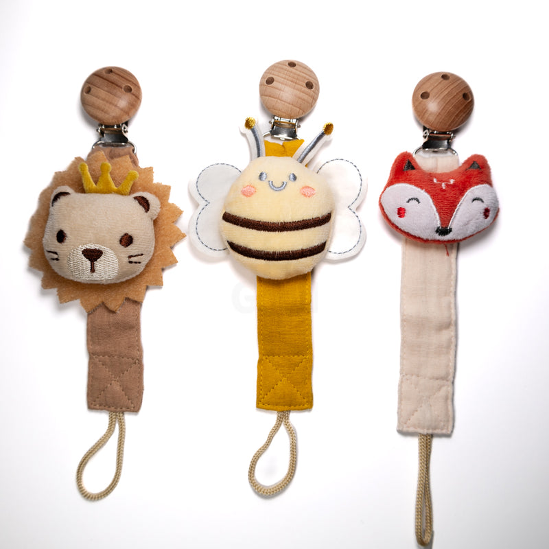 Three baby pacifier clips displayed side by side featuring a plush lion with a crown, a smiling bee with wings, and a fox face, each with a fabric strap and wooden clip on a white background, sold as a combo pack for babies and toddlers