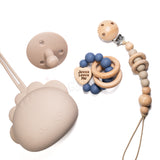 Collection of baby teething products including a silicone teether, wooden pacifier clip with beads, and a silicone teether with text on a white background.