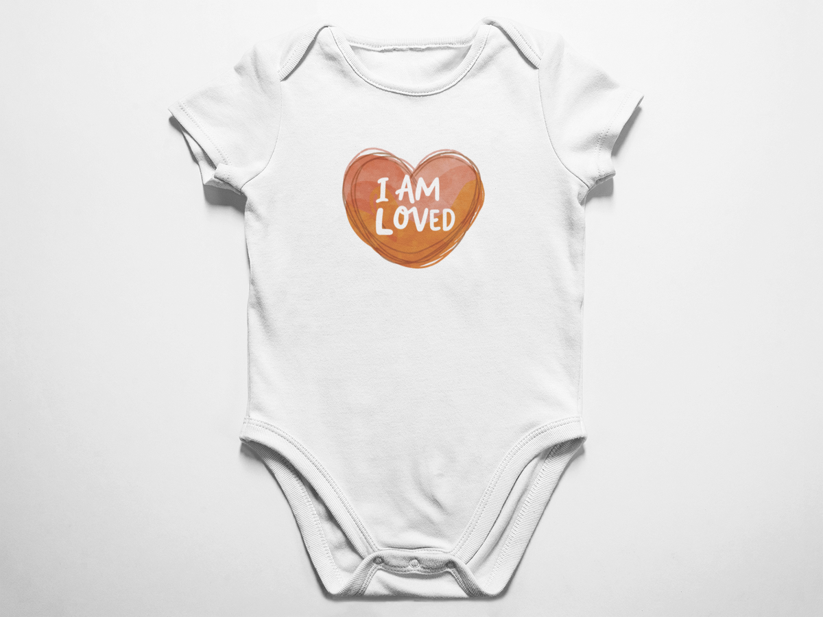 A clean flat lay view of a white baby onesie featuring a warm watercolor heart and the white text I am loved against a white background.