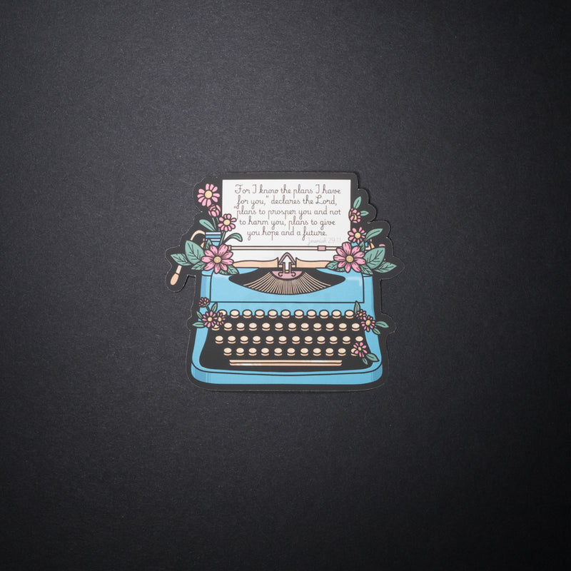 Jeremiah 29 11 typewriter sticker with blue typewriter, pink flowers, and Bible verse on black background