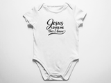 A clean flat lay view of a white baby onesie featuring the black text Jesus Loves Me This I know in a mix of cursive and classic typography against a white background.
