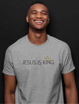 A smiling man wearing a heather gray t-shirt with the text 'JESUS IS KING' and a small gold crown graphic on the chest, set against a solid black background.