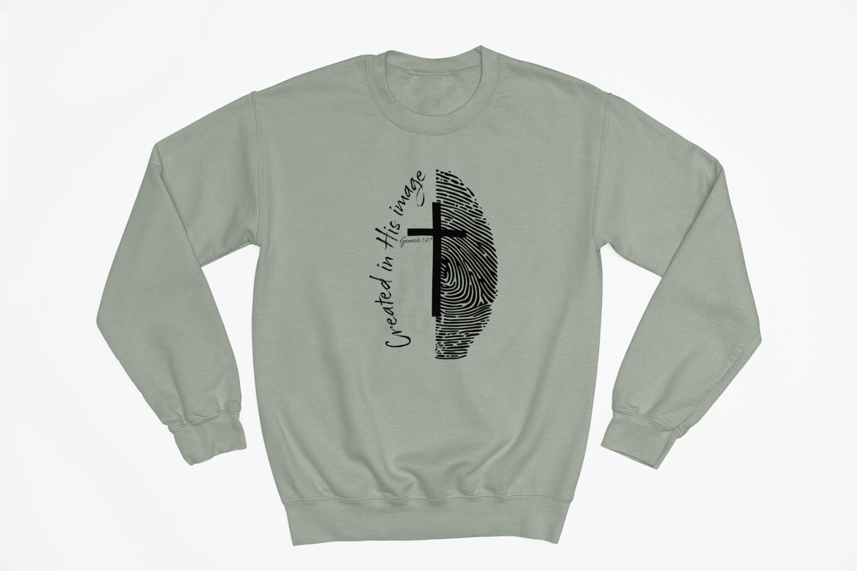 A sage green crewneck sweatshirt with a black graphic on the chest featuring a split fingerprint design, a cross, and the cursive text 'Created in His Image'.