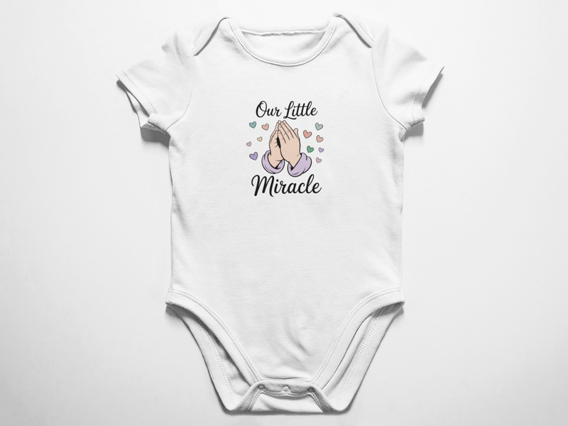 A clean flat lay view of a white baby bodysuit featuring the text Our Little Miracle with an illustration of praying hands surrounded by pastel hearts against a white background.