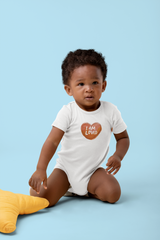 A sweet toddler boy wearing a white I am loved onesie sits playfully on a light blue background next to a yellow star pillow.
